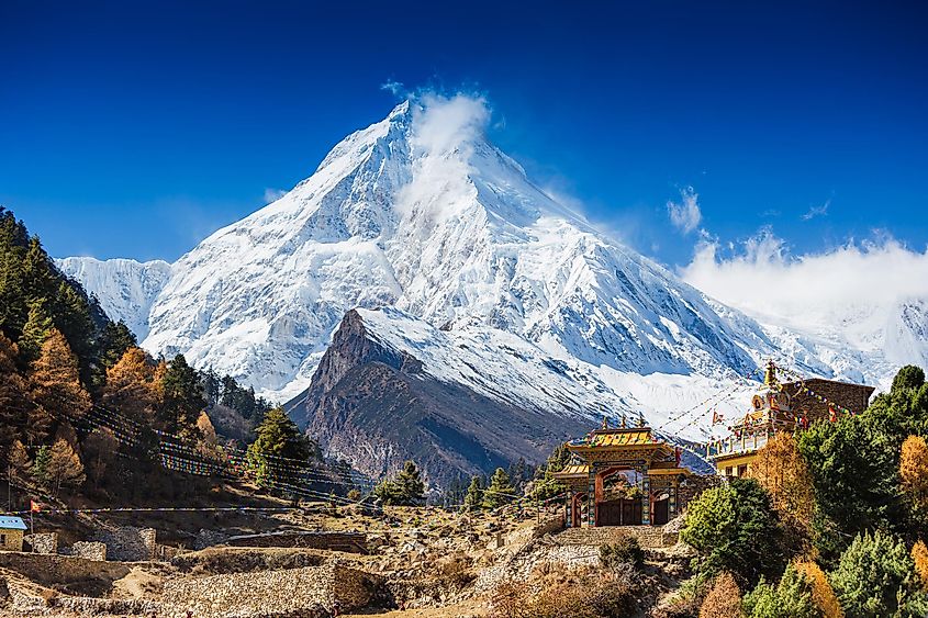 A giant snowy mountain soars above a small village with Buddhist shrines.
