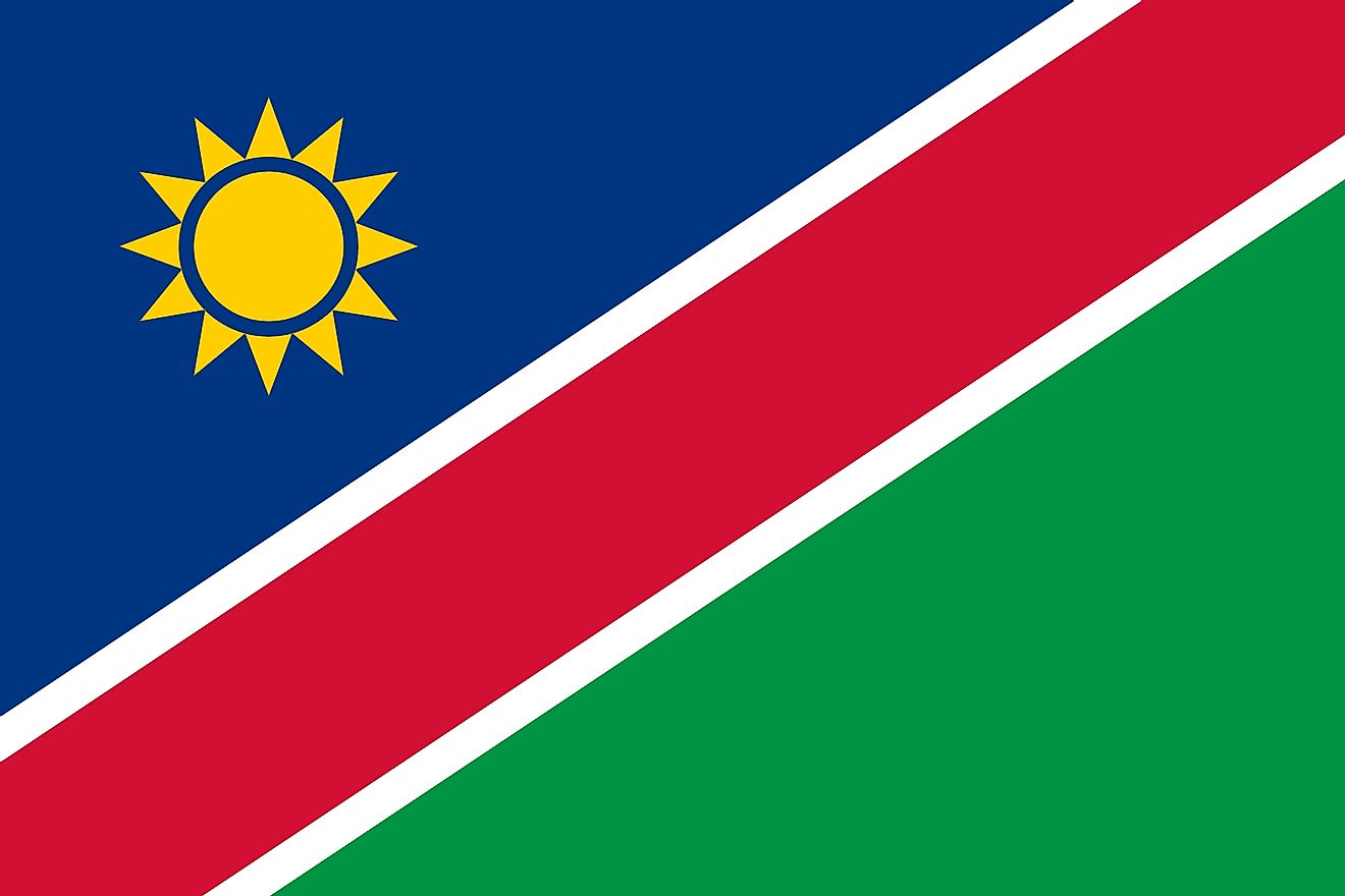 The flag of Namimbia consists of a wide red stripe edged by narrow white stripes dividing the flag diagonally from lower hoist corner to upper fly corner. The upper blue triangle is charged with golden sun while the lower triangle is plain green.
