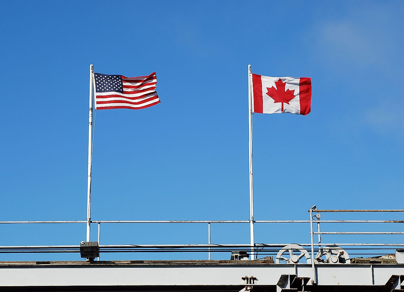 USA's and Canada's national flags fly at a US-Canada border. Image credit: Katherine Welles/Shutterstock.com