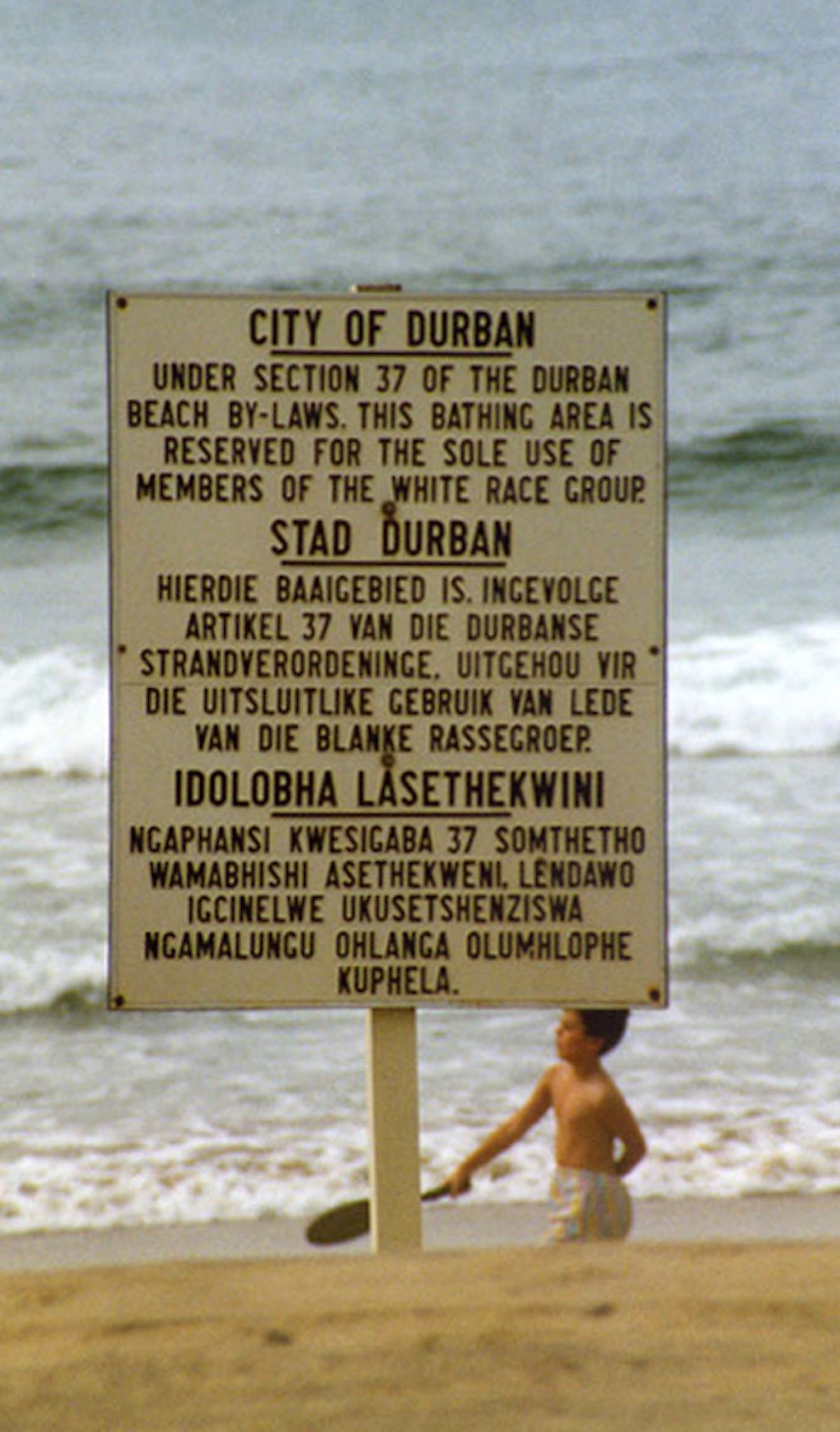 A sign reserving a Natal beach "for the sole use of members of the white race group" during the Apartheid era, in English, Afrikaans, and Zulu. Image credit: Guinnog/Wikimedia.org