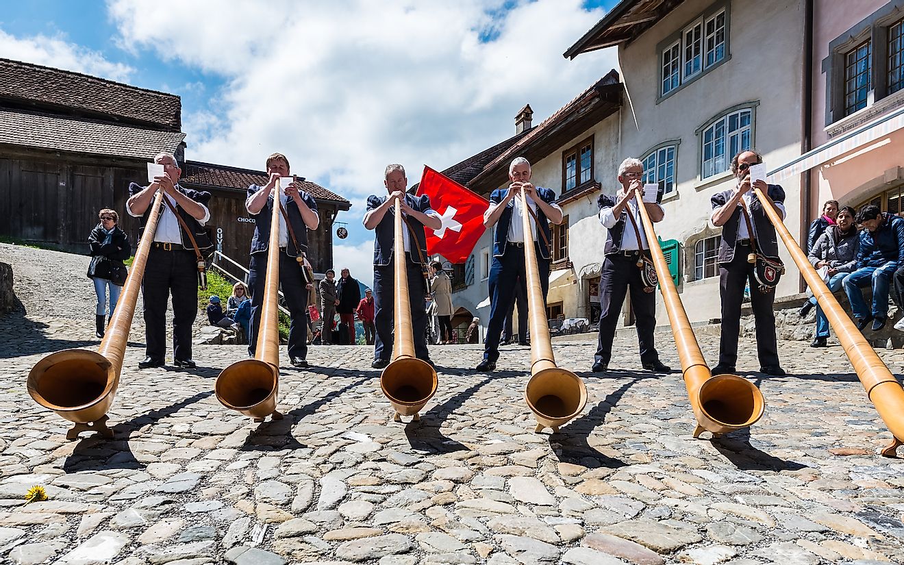 Swiss musicians play the alphorn, a traditional musical instrument on the main street of the Gruyere village. Image credit: eugeniek/Shutterstock.com