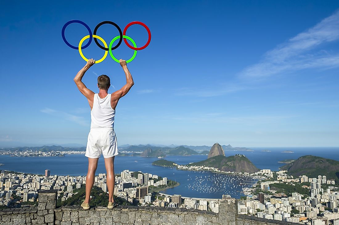 An athlete holds the Olympic rings while looking over Rio de Janeiro, Brazil. Editorial credit: lazyllama / Shutterstock.com.