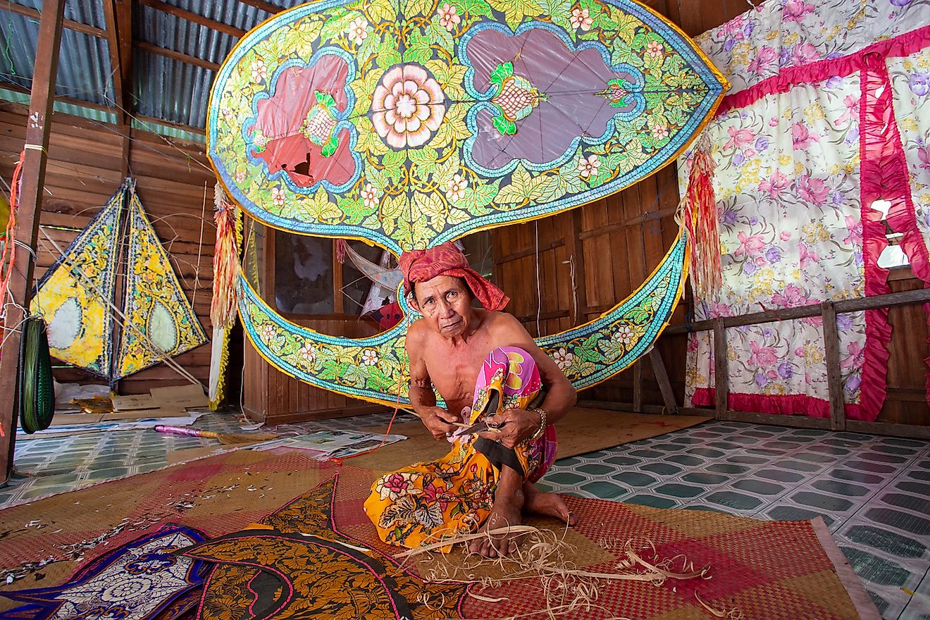 A traditional kite or "Wau" maker wearing batik sarung (Malay tradisional skirt) working on a kite in his workshop. Image credit: udeyismail/Shutterstock.com