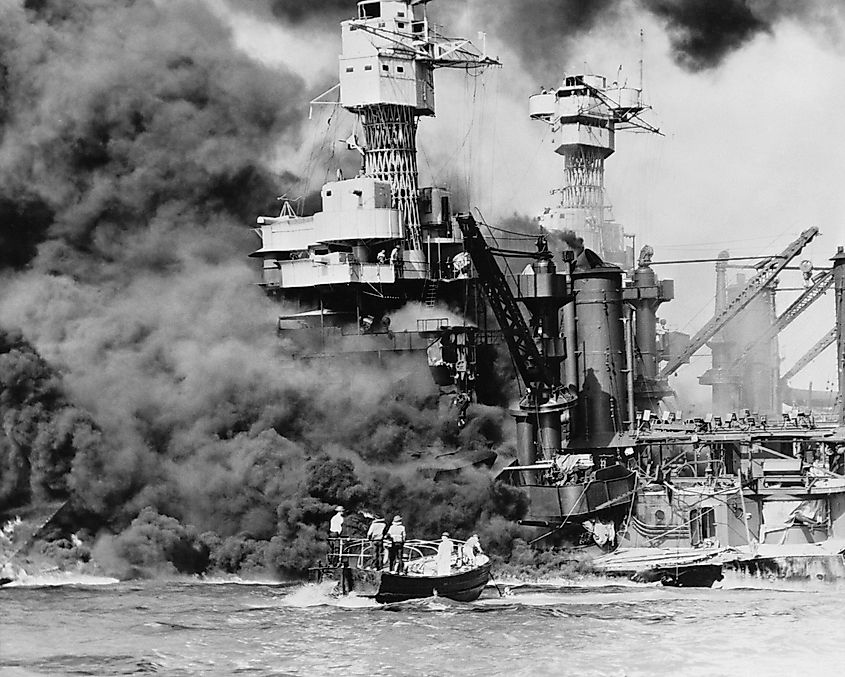 . A small boat rescues a seaman from the 31,800 ton USS West Virginia (BB-48), which is burning in the foreground.
