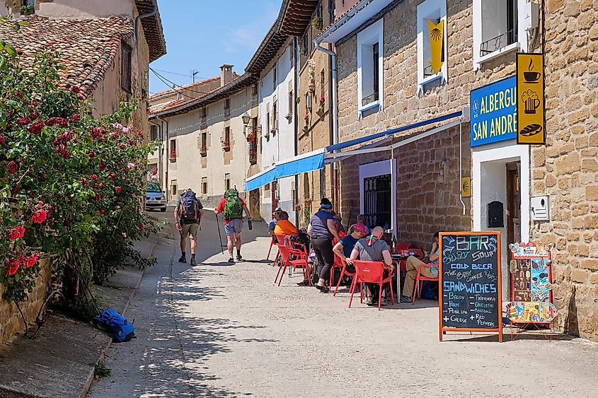 Backpackers are gathered outside of a Spanish hostel (albergue), enjoy the cute streetside patio on a sunny day