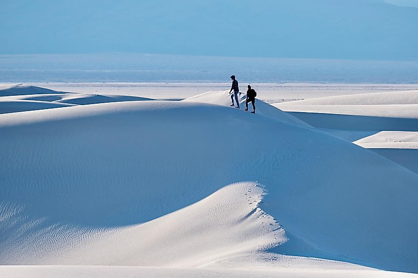 Two people walking on white sand dunes in distance. White Sands National Park. Alamogordo. New Mexico.