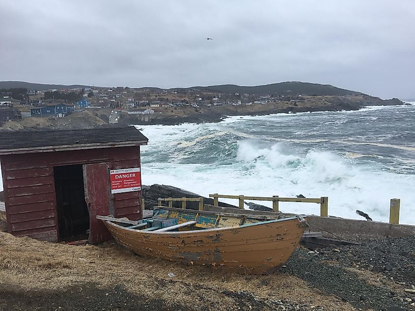 A weathered boat and red shed backdropped by a stormy ocean shoreline