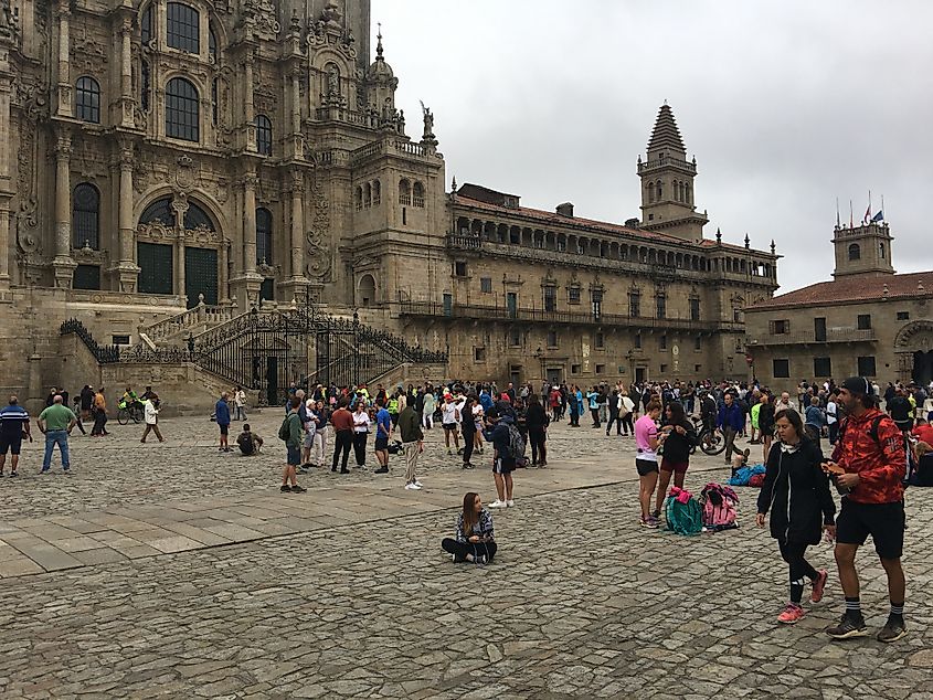 A crowd of tourists and backpackers gather in the square outside a large Spanish cathedral.