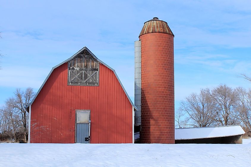 A shot of a Kansas Red Barn and Silo with snow on the ground with blue sky and tree's. That's north of Hutchinson Kansas USA
