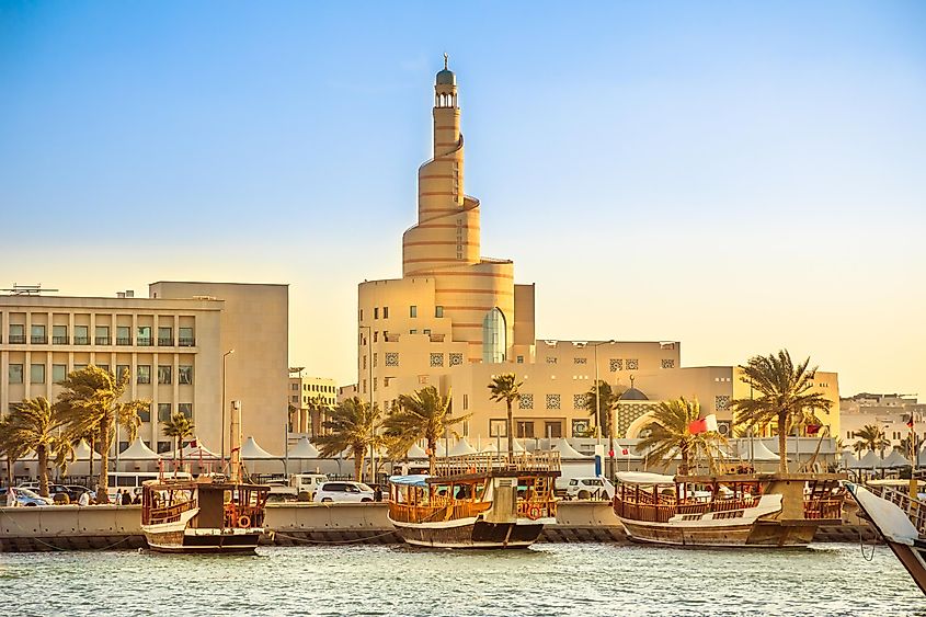 Traditional wooden dhow anchored at Dhow Harbor in Doha Bay, Qatar, with spiral mosque and minaret in the background.