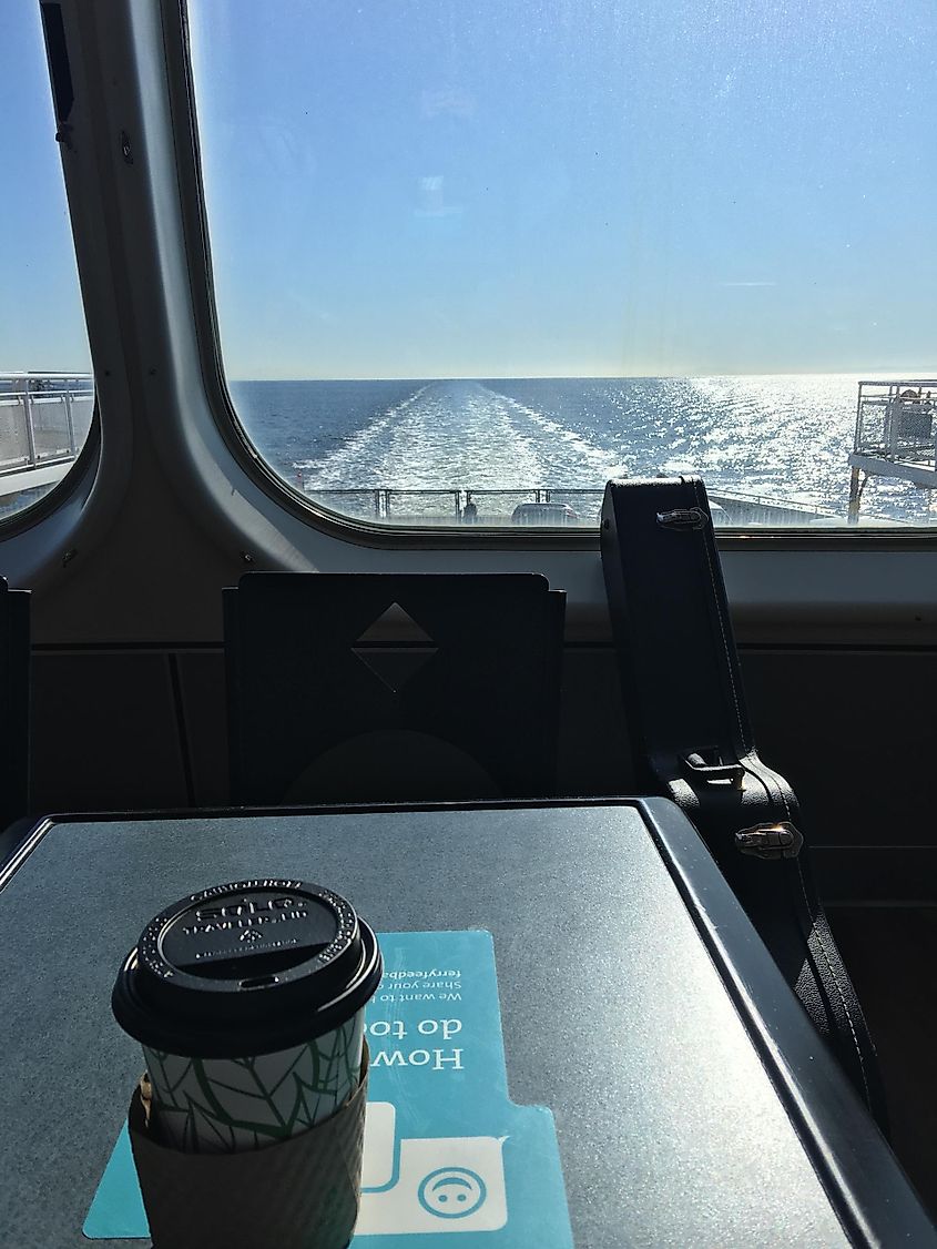 A table with a paper coffee cup next to a window on a ferry.