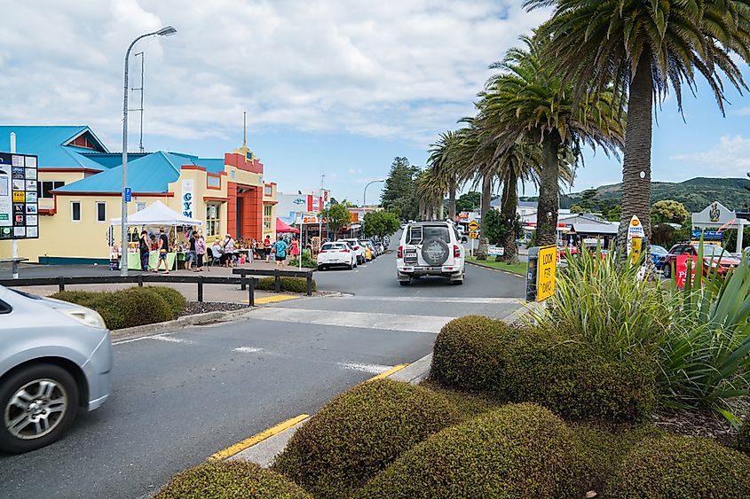 View along Bow Street in small town on busy summer Sunday morning vehicles, local market and people moving about in Raglan, New Zealand