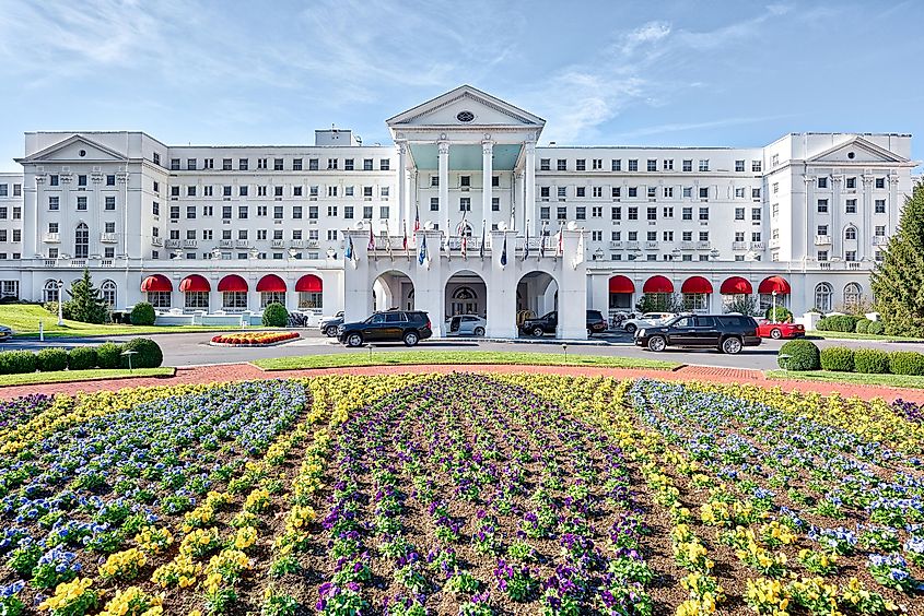 Exterior entrance of Greenbrier Hotel resort with landscaped flowers, lawn, and cars in White Sulphur Springs, West Virginia, USA.
