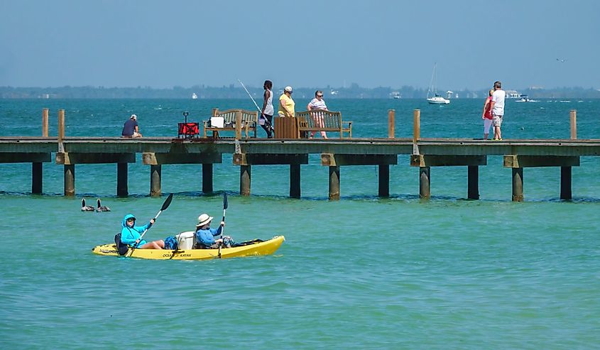 Two kayakers paddle near a public pier on Anna Maria Island