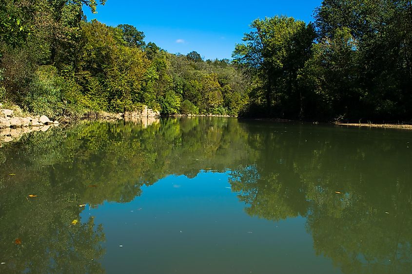 A blue sky reflects in the water of the Harpeth River.