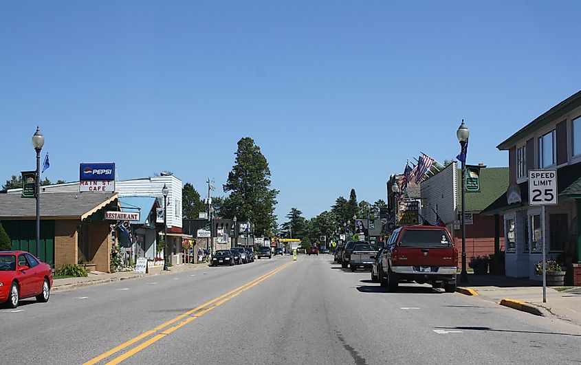 Downtown street of Three Lakes, Wisconsin, USA, with cars lined up along the sidewalks near stores.