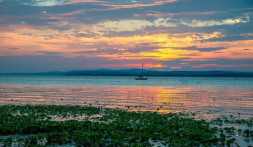 View of the sunrise and sailboat on Lake Champlain with the Green Mountains in the background in South Hero, Vermont.