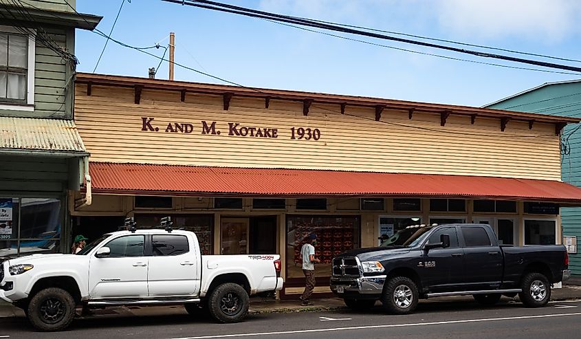 Photo of historic 1930ʻs building with man walking and parked trucks in this charming Big Island town.