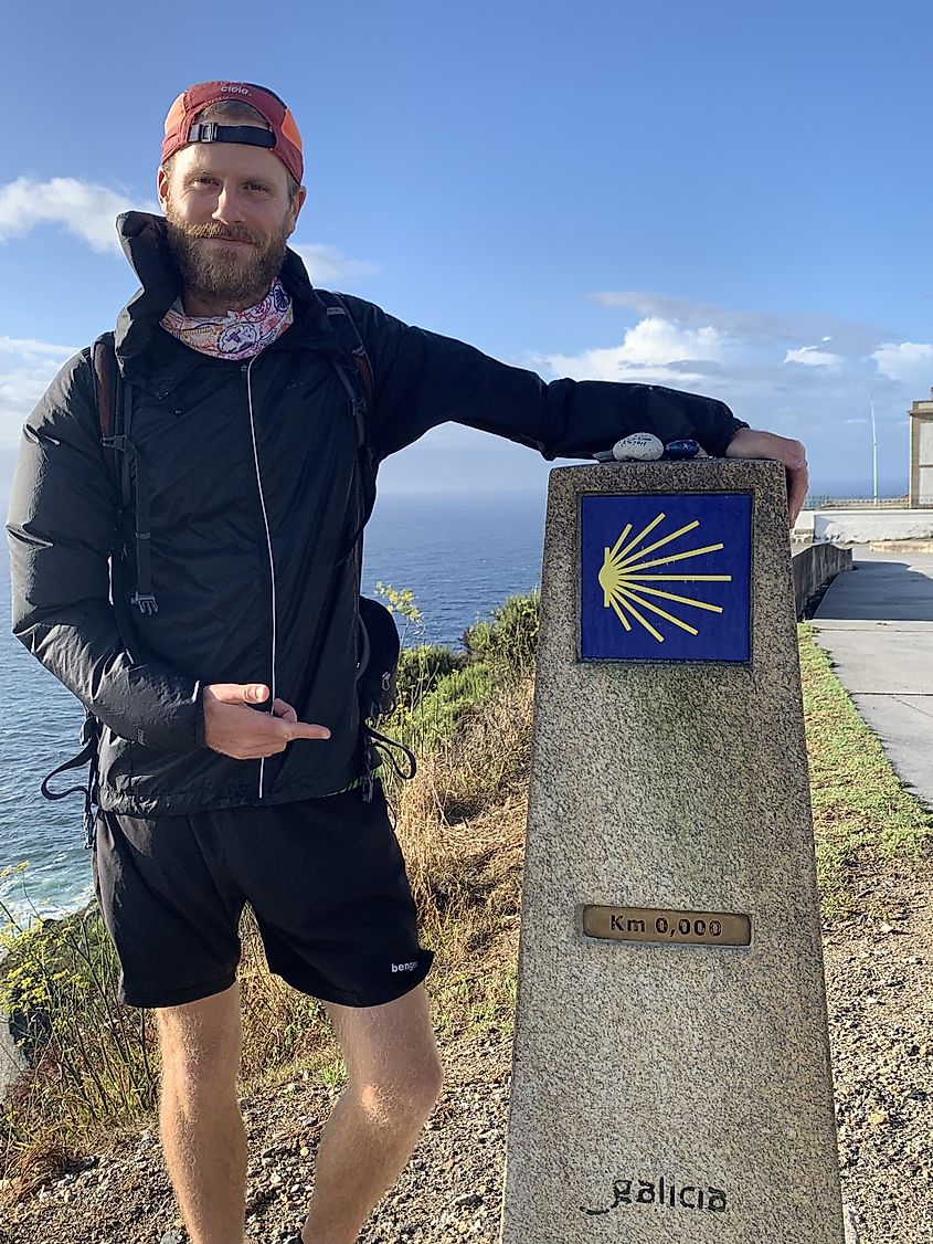 A male hiker poses next to a 0km distance marker on the Camino de Santiago. 