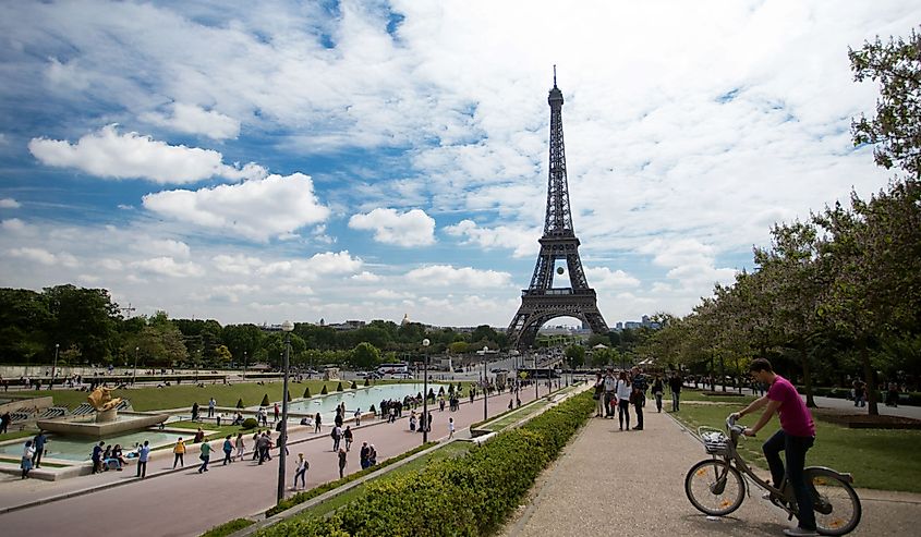 People walking in front of Eiffel Tower and man on the bicycle on the foreground. Bright blue sky with clouds in Paris, France