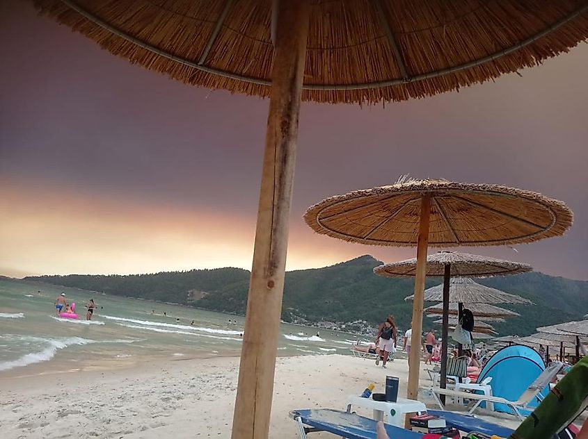 A beach in Greece, darkened by the black and orange sky created by the nearby wildfires. 