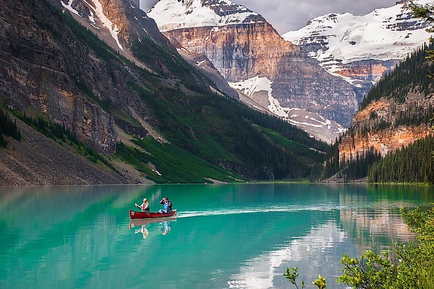 Red canoe floating in turquoise water at Lake Louise, Alberta, Canada. Couple canoeing together in the beautiful glacial lake at sunrise.