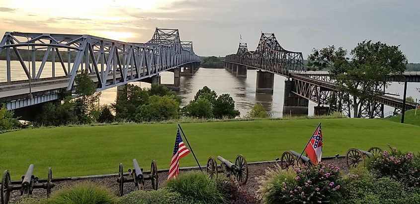 Two bridges crossing the Mississippi River in Vicksburg, Mississippi, contrasting old and new, railroad and highway, with the United States and State of Mississippi flags flying.