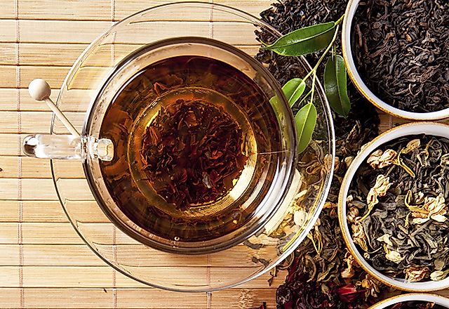 Multiple varieties of loose leaf tea next to a cup of brewed tea.
