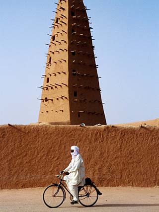 Robed Tuareg Man Cycling Past Minaret of Mud-Brick Grande Mosquee, Agadez, Niger