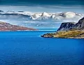The remote Bering Strait near Alaska features cold deep blue water, rugged northern mountains, dramatic clouds and pristine Arctic wilderness.