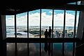 Couple standing in front of the large glass windows at One World Observatory, overlooking the New York City