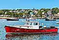 Harbor at Stonington, Maine, USA, features a vibrant red lobster boat in the foreground surrounded by scenic coastal beauty.