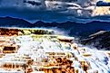 Travertine terraces at Mammoth Hot Springs, Yellowstone, under cloudy skies.
