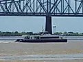 A ferry crosses the Mississippi River under a bridge in New Orleans, via Wirestock on iStock.com