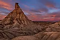 A stunning view of a unique rock formation in Bardenas Reales, Spain, under a vibrant sunset sky