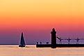 A vividly colorful twilight sky silhouettes a sailboat, people, and the lighthouse at South Haven, Michigan, on Lake Michigan.
