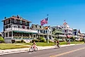 People bike and walk in front of traditional villas in Cape May, New Jersey, USA, on a sunny summer day.