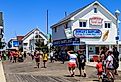 Stores, shops, and eateries attract visitors on the Ocean City boardwalk, Maryland. Image credit George Sheldon via Shutterstock