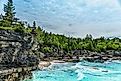 Backpackers taking a break on limestone cliffs before the rolling waves of Georgian Bay. A dense coniferous forest and overhead clouds form the backdrop. Image by Golden Shrimp via Shutterstock.com