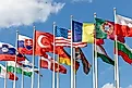 A group of flags from countries from around the world on flagpoles, fluttering in the wind against the backdrop of a blue sky.
