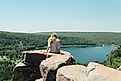 Editorial Photo Credit: Cavan-Images via Shutterstock. High angle of female sitting on cliff at Devil's Lake State Park, WI