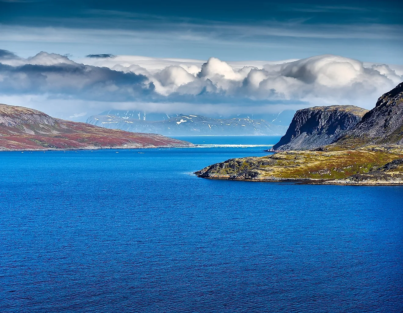 The remote Bering Strait near Alaska features cold deep blue water, rugged northern mountains, dramatic clouds and pristine Arctic wilderness.