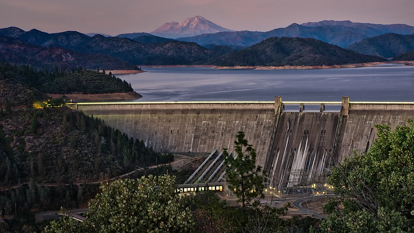 A picture of Shasta Dam with a lake and rocky mountains on the background during sunset. 