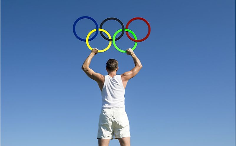 An athlete holds Olympic rings aloft against bright blue sky. Editorial credit: lazyllama / Shutterstock.com