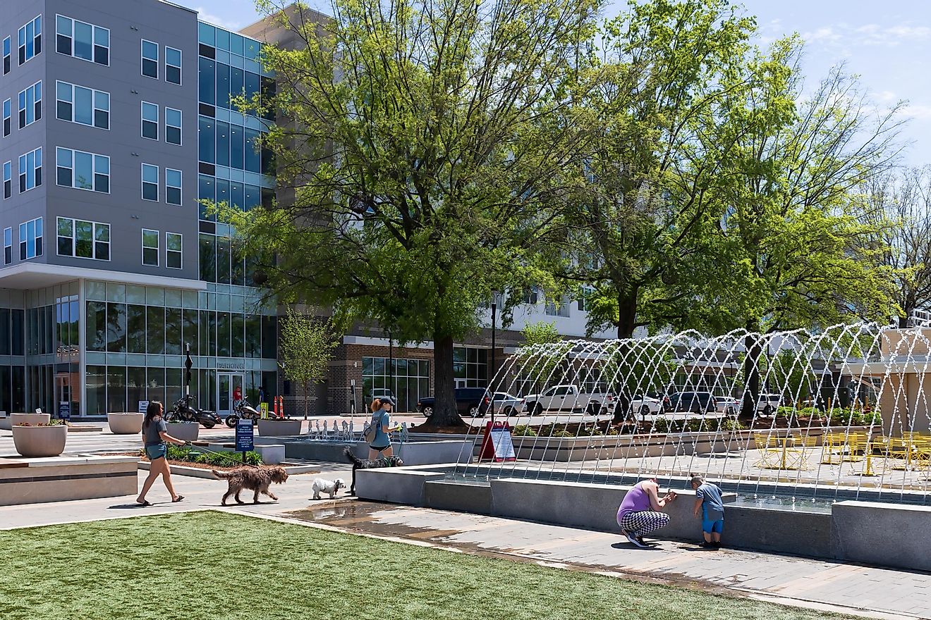Kannapolis, North Carolina: Women walking dogs and mother taking picture of small child around the water feature along West Avenue on a sunny, spring day.