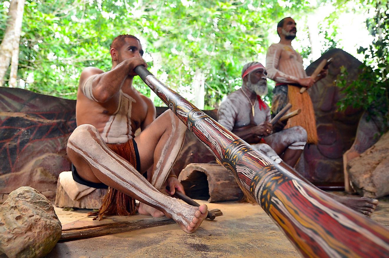 Australian Aboriginal men play Aboriginal music on didgeridoo and wooden instrument during Aboriginal culture show in Queensland, Australia. Image credit: ChameleonsEye/Shutterstock.com