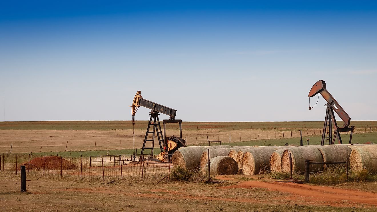 A scene from rural Oklahoma. Oil pumps and hay bales in the prairie.