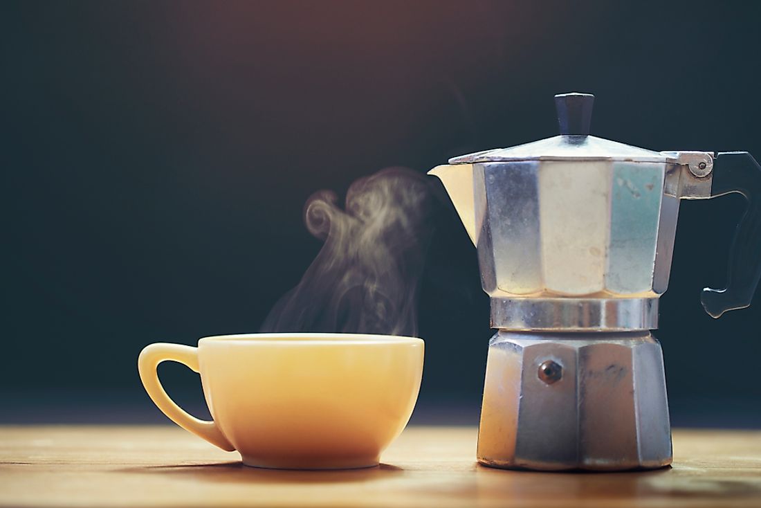 A cup of coffee next to a traditional coffee maker. 