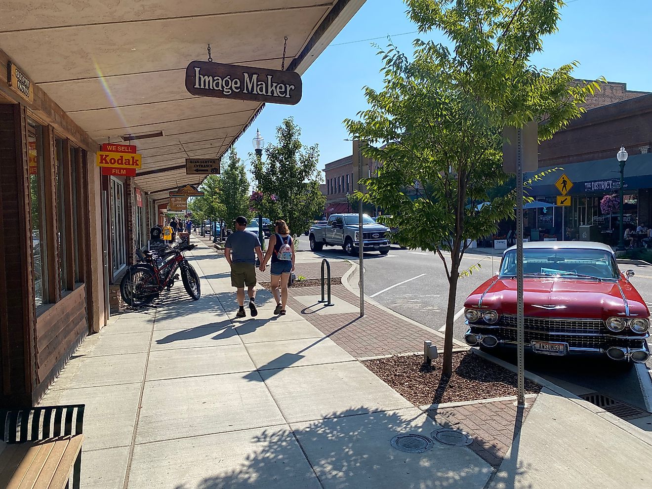 A couple walks past shops and a bright red old fashioned corvette on main street Sandpoint, ID