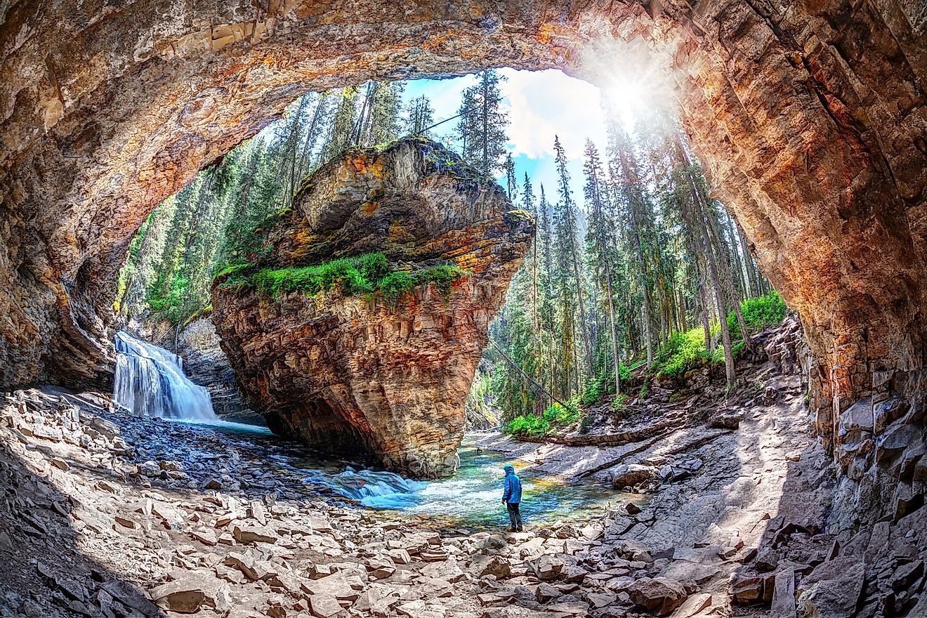 Hiker stands in awe of waterfall and limestone bedrock at a hidden cave in Johnston Canyon at Banff National Park.